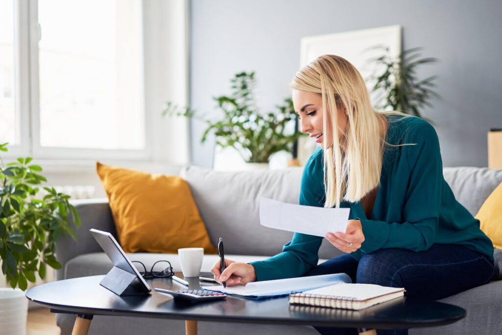 Smiling woman analysing bills filling tax documents while at sitting on sofa at home